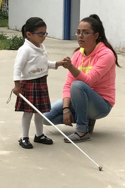 Student learning to use a cane with teacher guiding